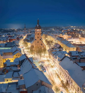 Aerial view of a snowy town center with a glowing church and illuminated streets at dusk
