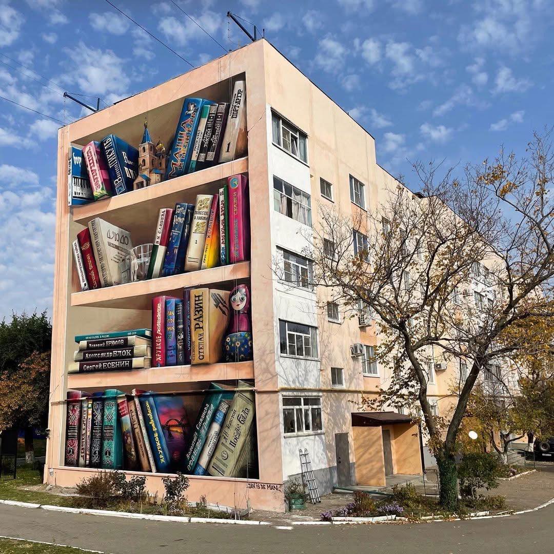 Multi-story apartment building with realistic painted bookshelf mural on side facade showing colorful book spines