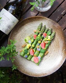 Gourmet asparagus dish with edible flowers and vegetables on a round plate on a wooden outdoor table
