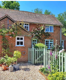 Red brick cottage with white windows, climbing roses, picket fence and garden path