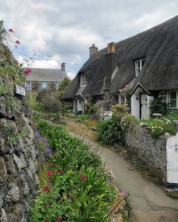 White thatched-roof cottage beside a narrow garden path with stone walls and flowering plants