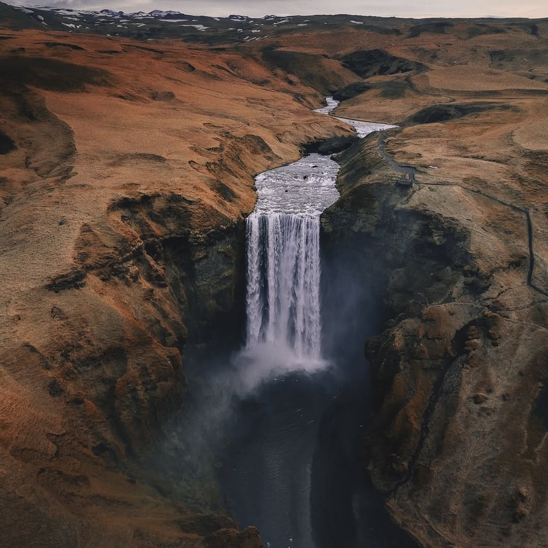 Waterfall dropping into a deep dark canyon among brown rocky hills
