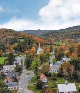 Aerial view of a small New England village with white church and autumn foliage on surrounding hills