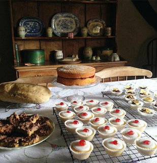 Assorted homemade baked goods and cakes on rustic wooden table with vintage dishes on shelves behind