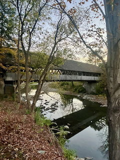 Red covered bridge over peaceful river with autumn foliage and reflections in Woodstock Vermont