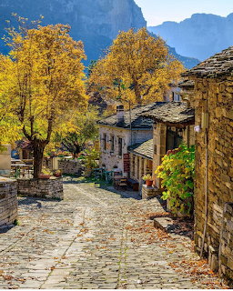 Cobblestone lane winding through stone village buildings with autumn foliage and mountains behind