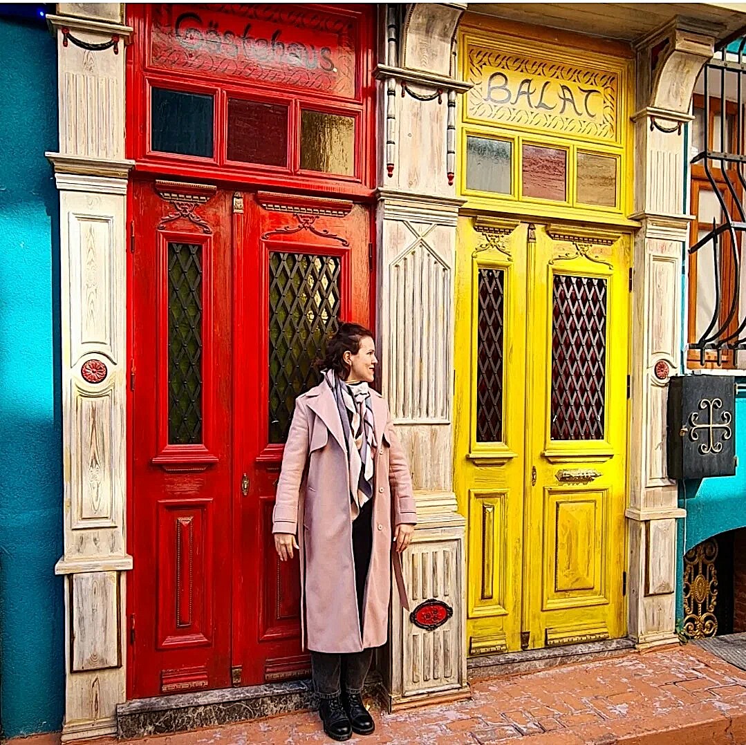 Woman standing between ornate red and yellow doors on a colorful old building facade