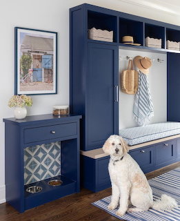White dog sitting in navy blue coastal mudroom with built-in storage and bench