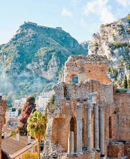Ancient brick Roman theater ruins with columns in Sicily hillside town with mountain background