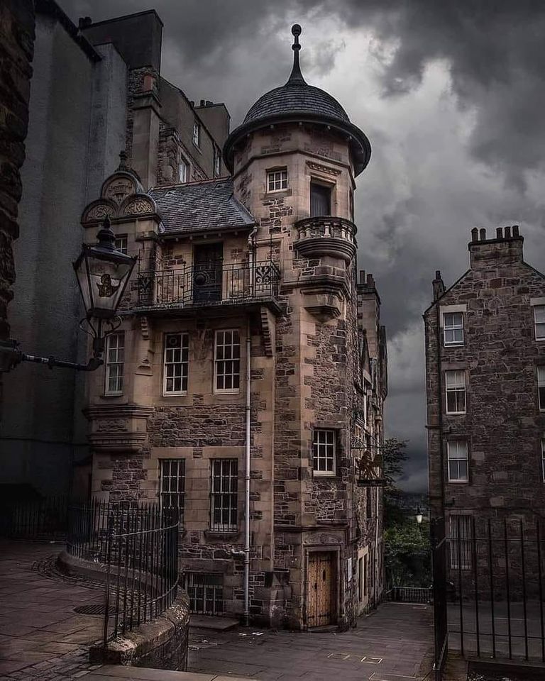 Historic stone building with turret tower under dark stormy clouds in Edinburgh