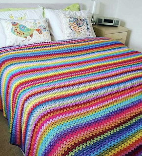 Colorful rainbow striped crochet blanket covering a bed with decorative pillows