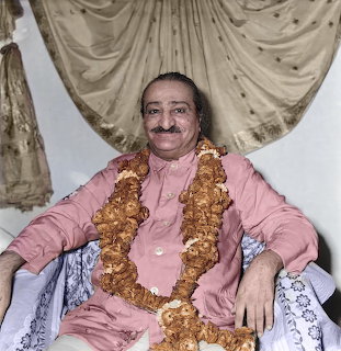 Seated man in pink clothes wearing flower garlands, smiling in an indoor portrait