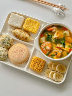 White compartment tray with shrimp soup, dumplings, mooncakes, corn, noodles, and banana slices