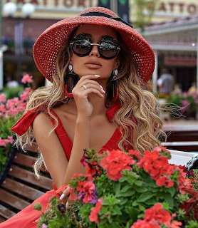 Woman in red straw hat and sunglasses with red geraniums at outdoor café