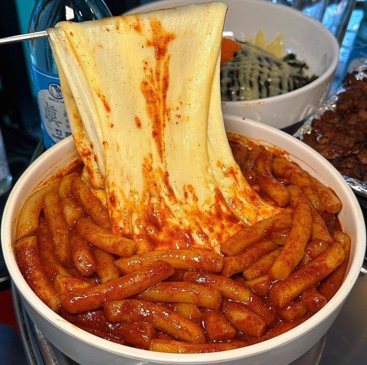 Chopsticks lifting chewy Korean rice cakes coated in glossy red spicy sauce from a bowl