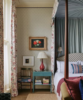 Cozy bedroom with a curtained bed, side table, lamp, chair, and framed artwork