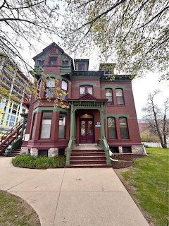 Victorian three-story burgundy house with ornate details and front porch surrounded by lawn and bare trees