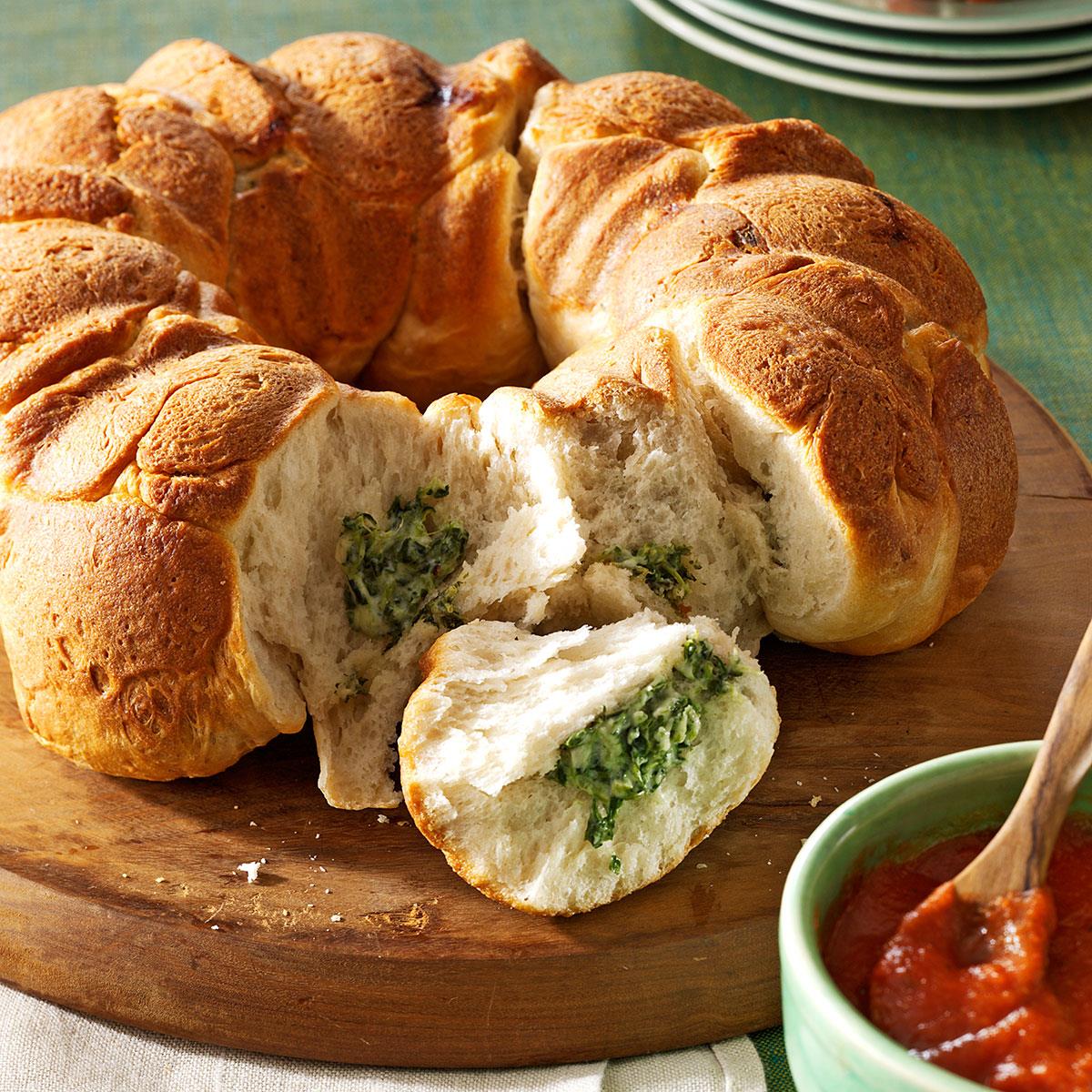 Sliced spinach-filled braided bread ring on wooden board with green plates and red sauce bowl