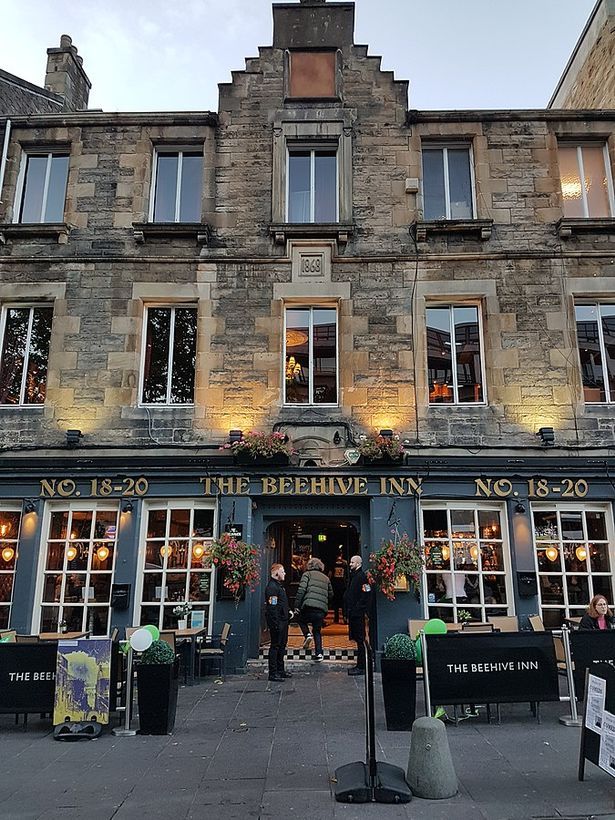 Front view of The Beehive Inn, a historic stone pub building in Edinburgh with people standing at entrance