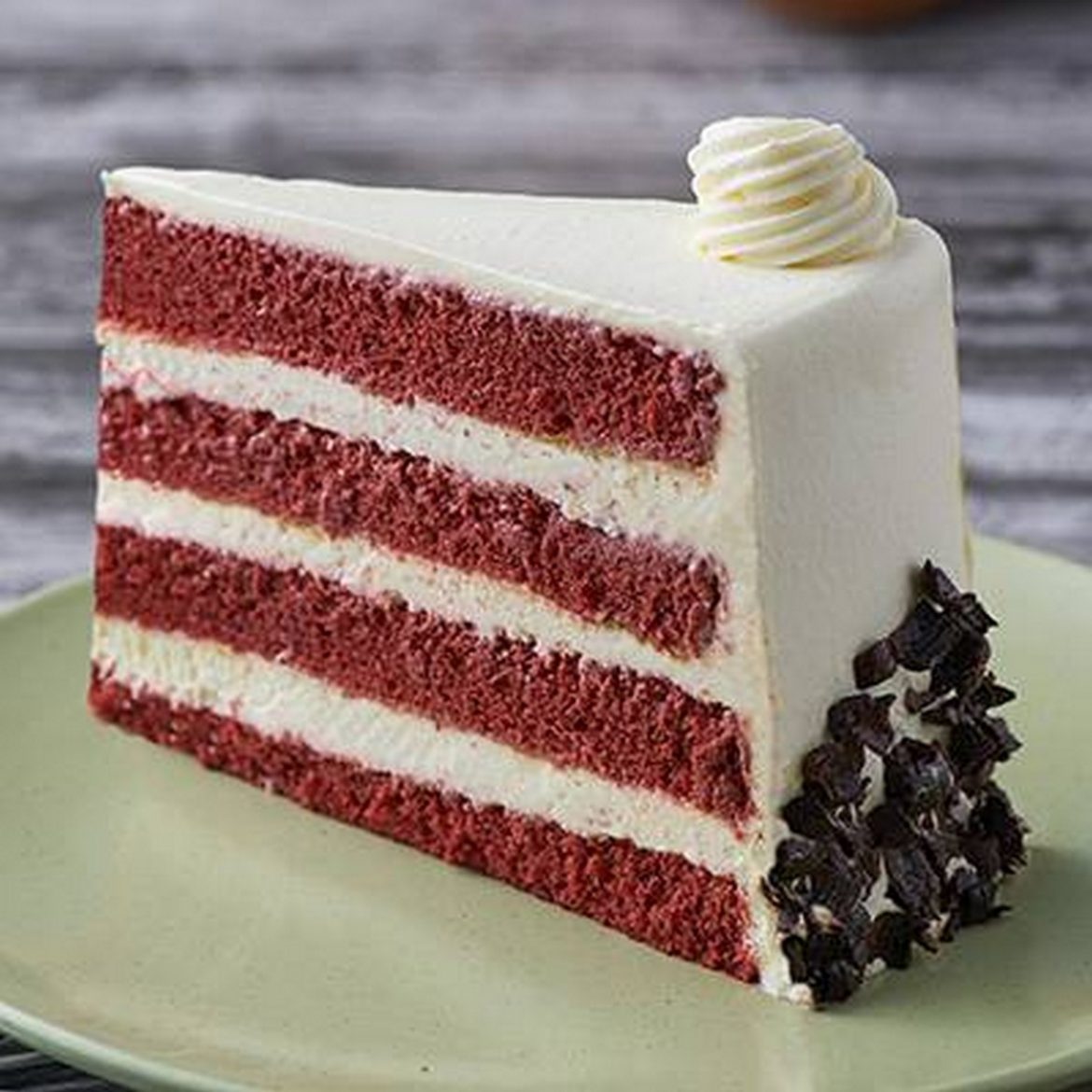 Slice of red velvet layer cake with white frosting and chocolate pieces