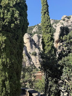 Montserrat monastery building set against tall rocky mountain formations with cypress trees in foreground