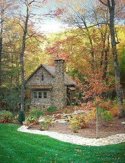 Stone cottage with chimney surrounded by fall foliage and a green lawn with gravel path