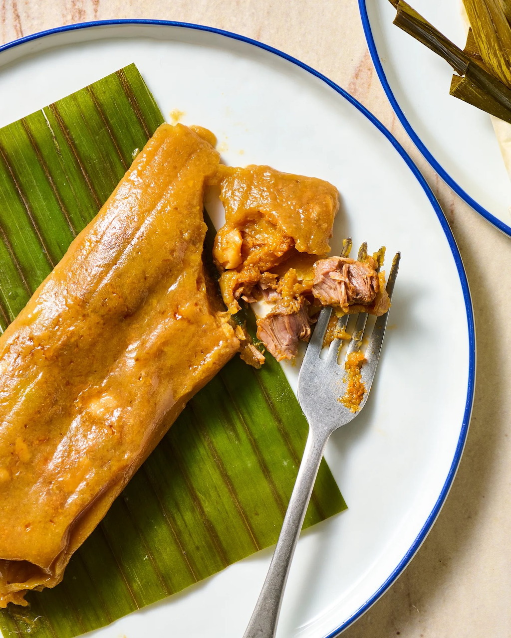 Puerto Rican pasteles on a white plate with banana leaf, fork holding a piece of the meat-filled dish