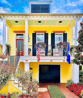 Bright yellow house with white porch, black shutters, and colorful flower garden in front