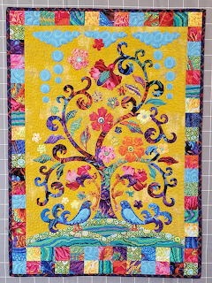 Quilted wall hanging with whimsical tree, birds, and colorful patchwork border