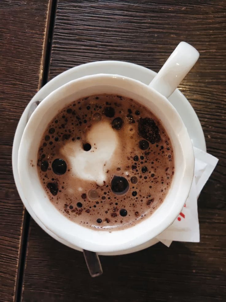 Overhead view of cappuccino with foam in white cup on dark wood table