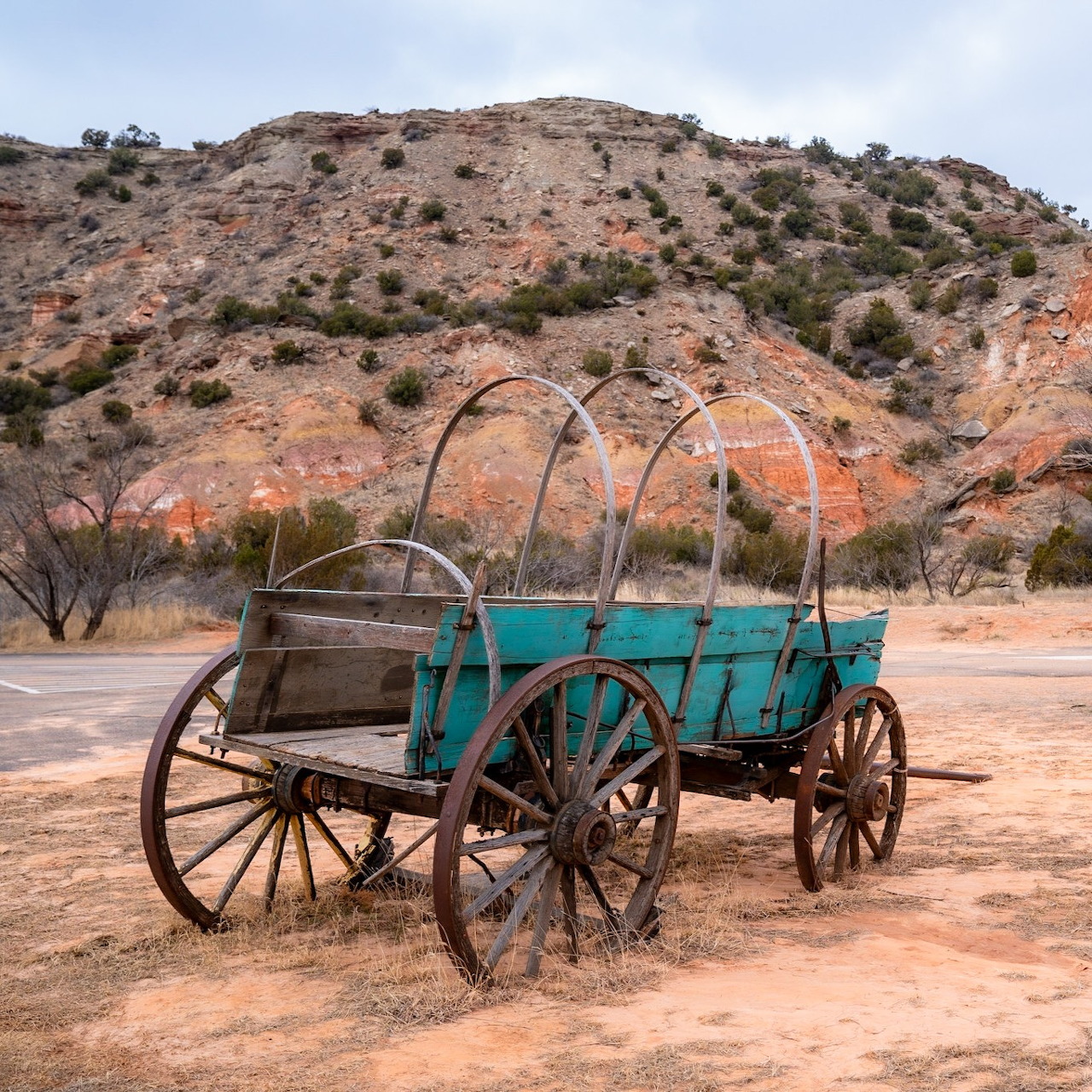 Weathered turquoise wooden wagon on dirt ground with arid mountain hillside in background