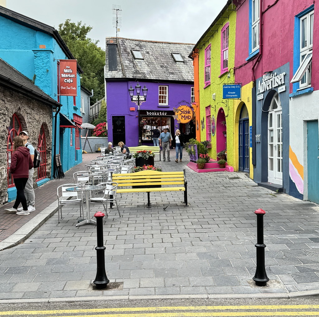 Colorful street with bright pink, purple, blue and yellow buildings and pedestrians on cobblestone pavement