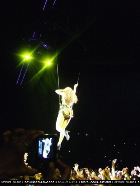 Beyoncé hanging on a rope high above the crowd during a live concert with green stage lights