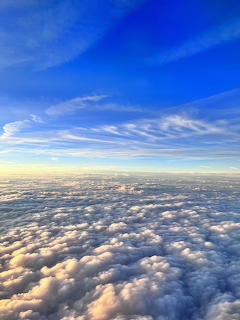 Aerial view of sunset-lit clouds below blue sky with wispy white clouds