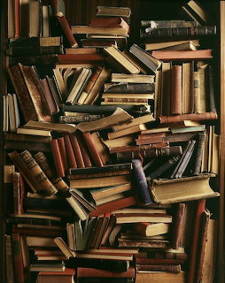 A dense stack of old books piled closely together in a dark interior