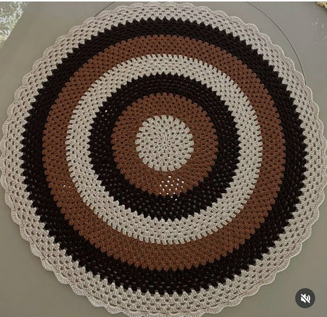 Round crocheted doily with brown, black and cream concentric circles and scalloped edge on neutral background