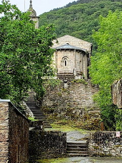 Romanesque stone church with rounded apse on a hill reached by stone stairs surrounded by green trees