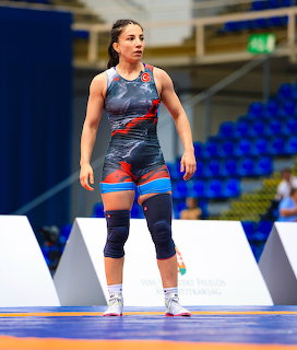 Female wrestler in blue and red singlet standing on a wrestling mat in an indoor sports arena