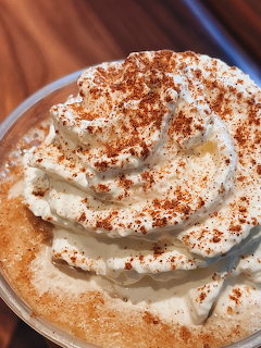 Coffee topped with swirled whipped cream and cinnamon powder in white cup