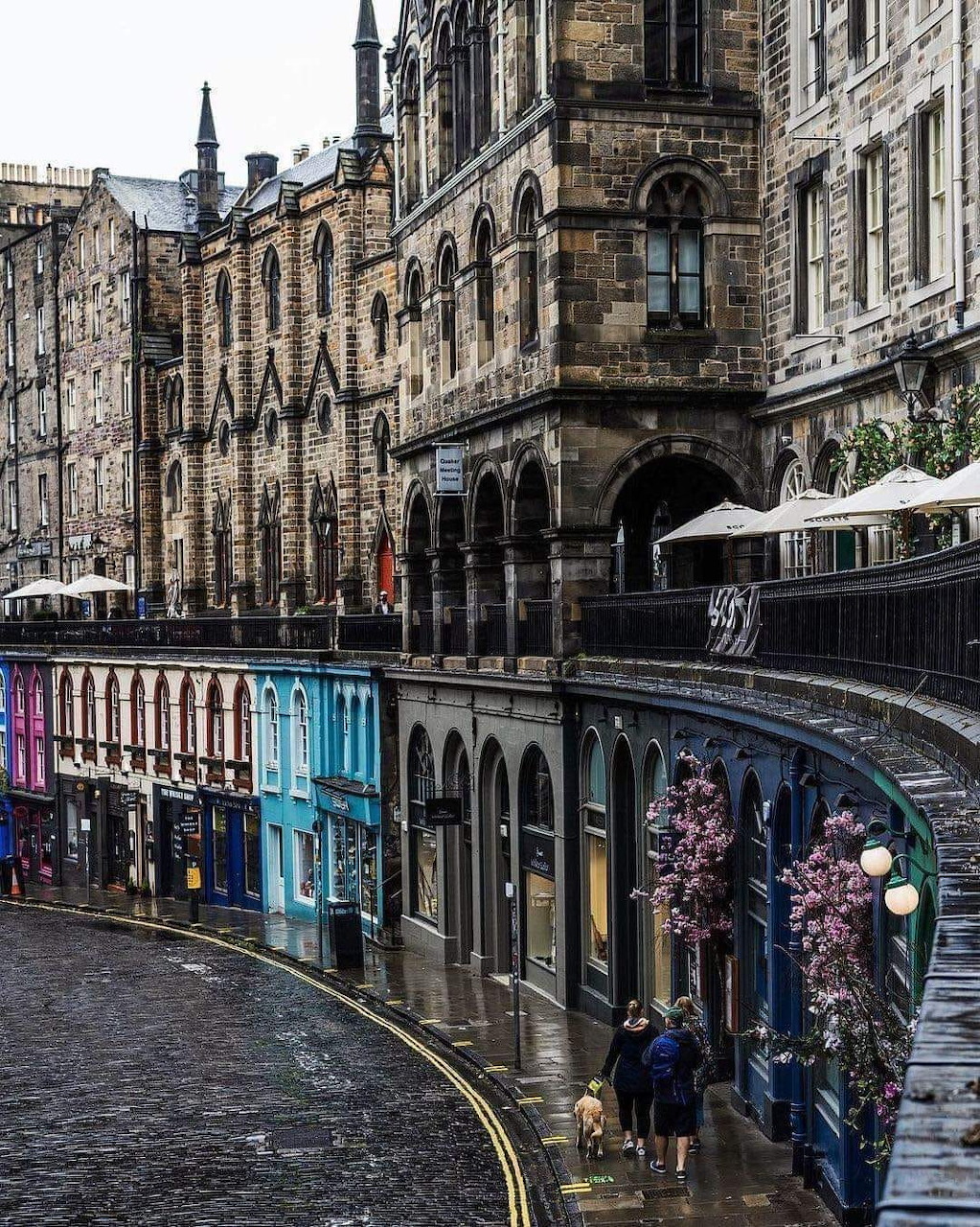 Curved cobblestone street with colorful shops and historic buildings in Edinburgh, Scotland