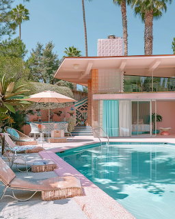 Pink mid-century modern house with turquoise pool, lounge chairs, umbrella, and palm trees