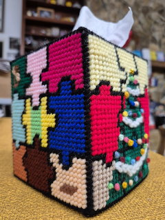 Handcrafted needlepoint tissue box cover with multicolored geometric designs and floral motifs on beige and brown backgrounds