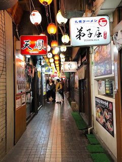 Narrow Japanese alley with hanging lanterns, restaurant signs, and a tiled walkway