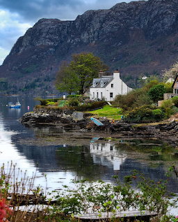 White cottage by a calm lake with mountain backdrop and water reflections