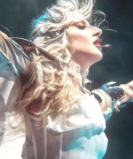 Digital art of a blonde woman with flowing hair and outstretched arms in glowing light
