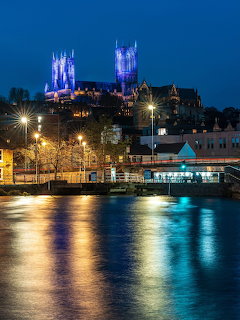 Lincoln Cathedral lit up in blue at night with river reflections and street lights in the foreground