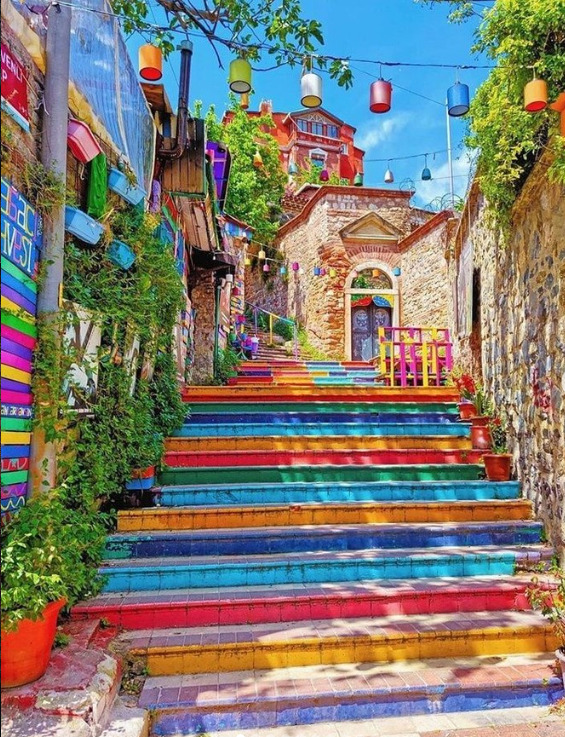 Rainbow-painted stairs on a narrow coblestone street with colorful buildings and hanging lanterns
