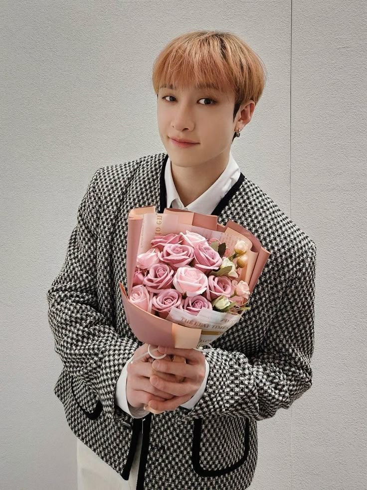 Young man with blonde hair holding a pink rose bouquet in a houndstooth jacket