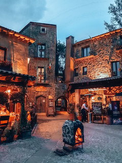 Medieval stone village square with warm lighting at dusk, old stone buildings and a glowing fireplace