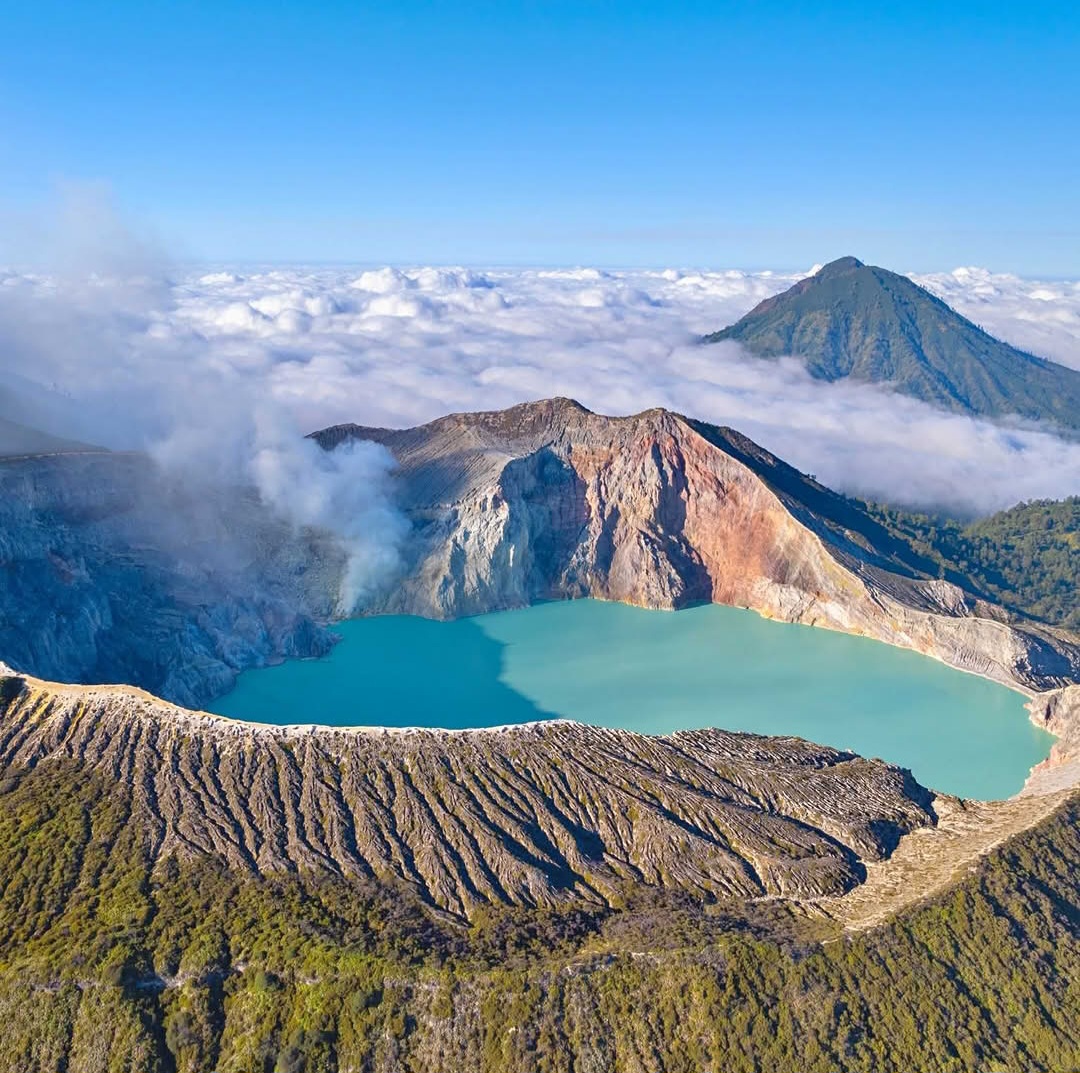 Turquoise volcanic crater lake surrounded by mountains and clouds in Indonesia